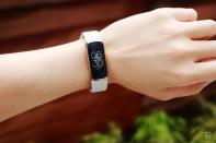 <p>Front view of the Fitbit Luxe with a light pink silicone band on a wrist against a dark brown background with some greenery. The screen shows the time is 6:30pm.</p> 