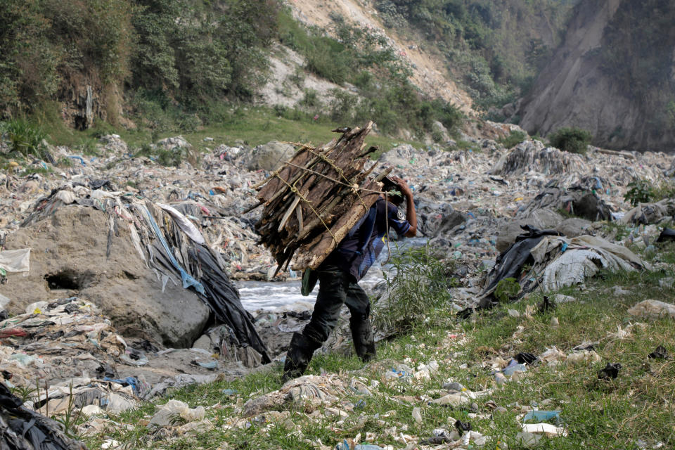 05 April 2023, Guatemala, Guatemala-Stadt: A man carrying wood on his back walks past mountains of garbage on the banks of the Rio Las Vacas. The river runs through an open landfill that, according to Hidrovacas, receives around 3,000 tons of garbage every day. Photo: Alejandro Balan/dpa (Photo by Alejandro Balan/picture alliance via Getty Images)