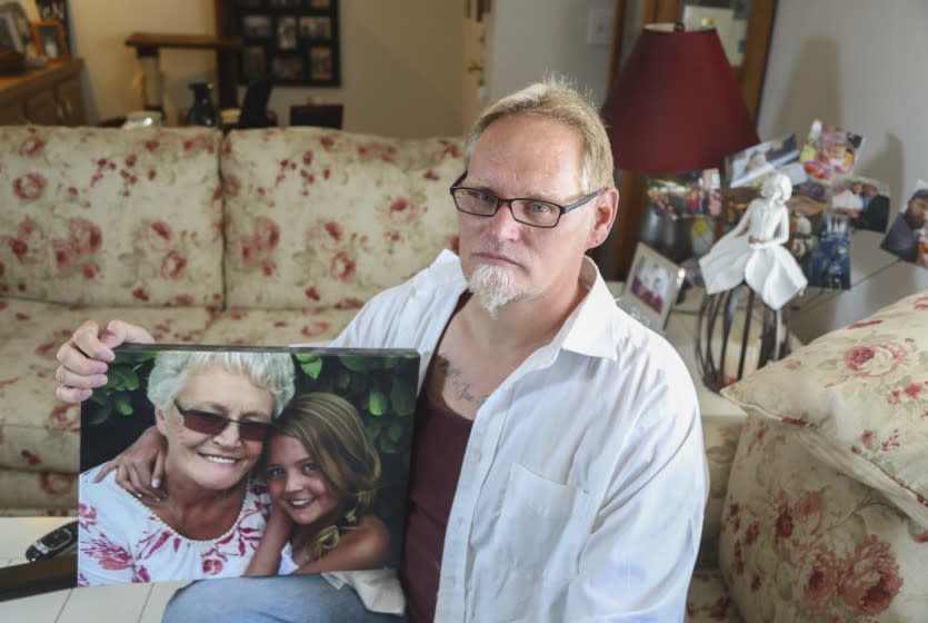 Chuck Beckner poses for a photo with a picture of his mother and niece at his home on July 17, 2020 in El Cajon, California. Beckner's mother Billy Sue Matcke, whose name is tattooed on his chest (tattoo seen in photo) died of COVID-19 shortly after going back to work as an Uber and Lyft driver. Unrelated to the story, his niece Summer Ellen "Elle" Tudor (young girl in photo) has also passed.