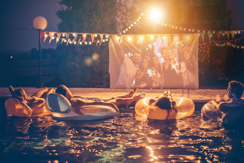 group of people watching a movie while sitting in inflatables in the pool at night