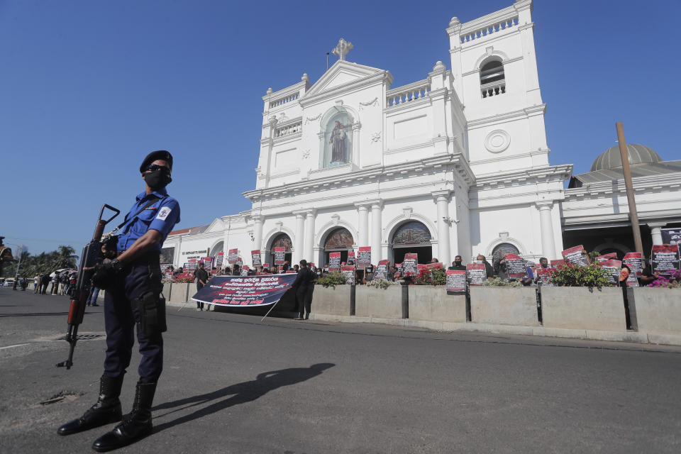 A policeman guards as Catholic devotees hold placards during a protest demanding justice for the 2019 Easter Sunday bomb attack victims out side the St. Anthony's church, one of attack sites, in Colombo, Sri Lanka, Sunday, March 7, 2021. (AP Photo/Eranga Jayawardena)