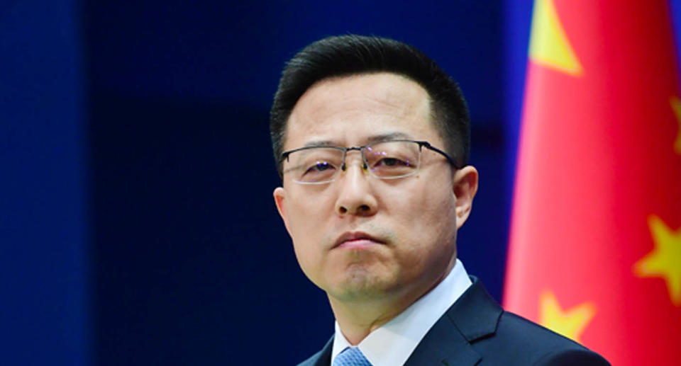 Zhao Lijian wears a suit at a press conference in front of a China flag.