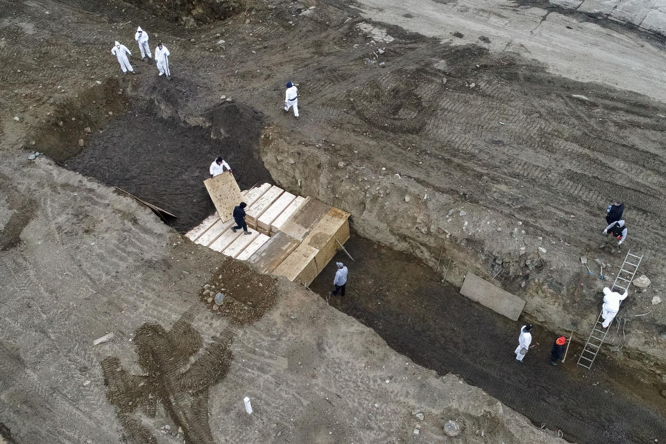 Workers wearing personal protective equipment bury bodies in a trench on Hart Island, Thursday, April 9, 2020, in the Bronx borough of New York. On Thursday, New York City’s medical examiner confirmed that the city has shortened the amount of time it will hold on to remains to 14 days from 30 days before they will be transferred for temporary internment at a City Cemetery. Earlier in the week, Mayor Bill DeBlasio said that officials have explored the possibility of temporary burials on Hart Island, a strip of land in Long Island Sound that has long served as the city’s potter’s field. (AP Photo/John Minchillo)