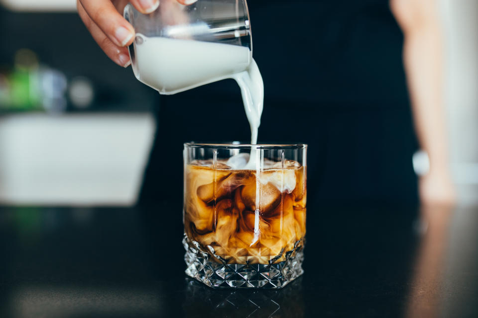 person adding milk to their homemade iced coffee