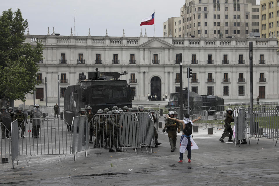 An anti-government protester opens his arms toward police guarding La Moneda presidential palace in Santiago, Chile, Wednesday, Oct. 23, 2019. Protesters have taken to the streets as an apology from the president and promises of reform failed to quell turmoil that has led to looting, rioting and at least 18 deaths. (AP Photo/Rodrigo Abd)