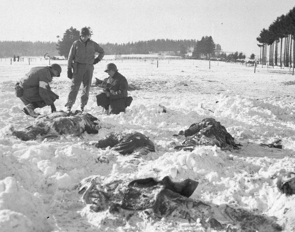 FILE - In this Jan. 1945 file photo, American soldiers check for identification on the bodies of dead U.S. troops shot by German troops near Malmedy, Belgium during World War II's Battle of the Bulge. It was 75 years ago that Hitler launched his last desperate attack to turn the tide for Germany in World War II. At first, German forces drove so deep through the front line in Belgium and Luxembourg that the month-long fighting came to be known as The Battle of the Bulge. When the Germans asked one American commander to surrender, the famous reply came: “Nuts!" By Christmas, American troops had turned the tables on the Germans. Veterans are heading and on Monday, Dec. 16, 2019 when they will mix with royalty and dignitaries to mark perhaps the greatest battle in U.S. military history. (AP Photo, File)