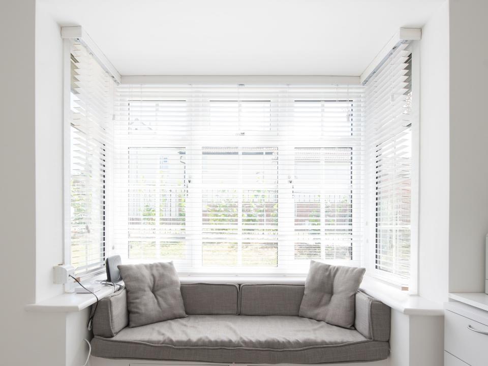 Window treatments with white trim and white blinds behind gray seat and pillows