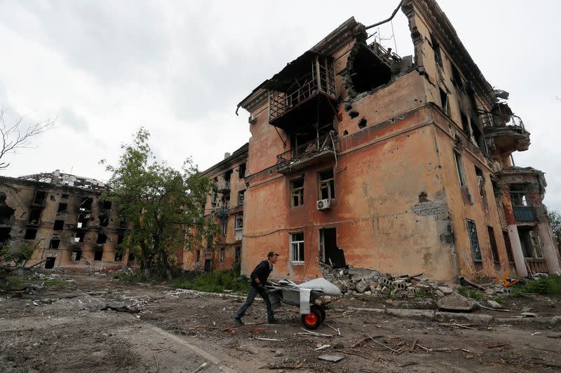 Un residente local empuja una carretilla frente a un edificio de apartamentos fuertemente dañado en Mariúpol