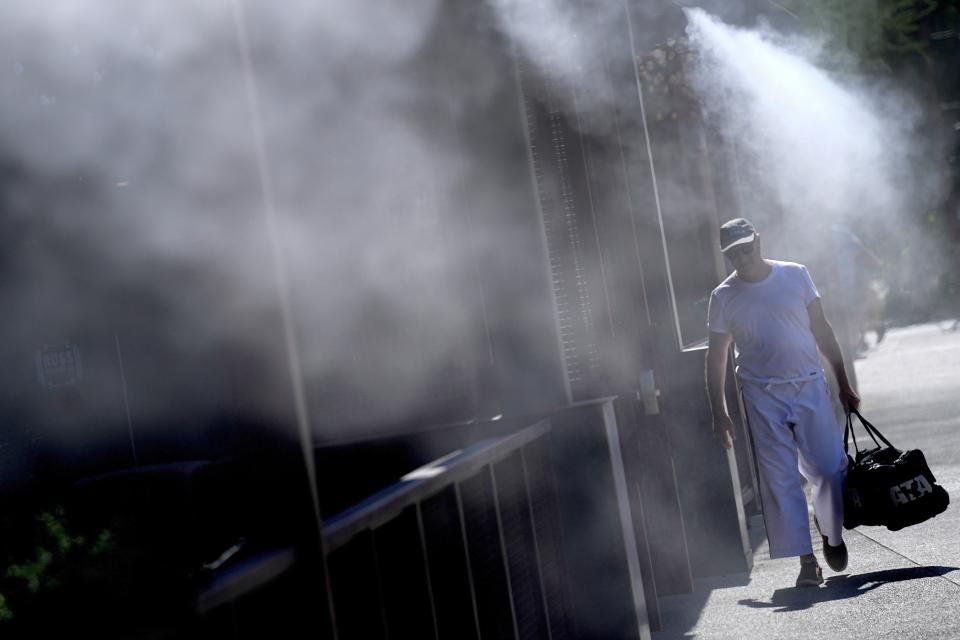 FILE - A man walks along a sidewalk under the misters, July 14, 2023, in downtown Phoenix. (AP Photo/Matt York, File)