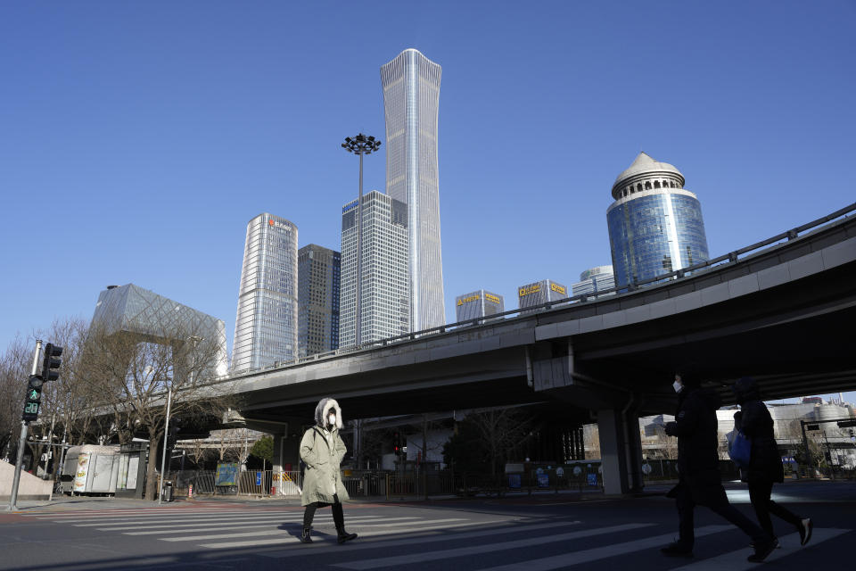 A resident crosses a quiet street near the Central Business District skyline in Beijing, Tuesday, Dec. 13, 2022. Some Chinese universities say they will allow students to finish the semester from home in hopes of reducing the potential of a bigger COVID-19 outbreak during the January Lunar New Year travel rush. (AP Photo/Ng Han Guan)