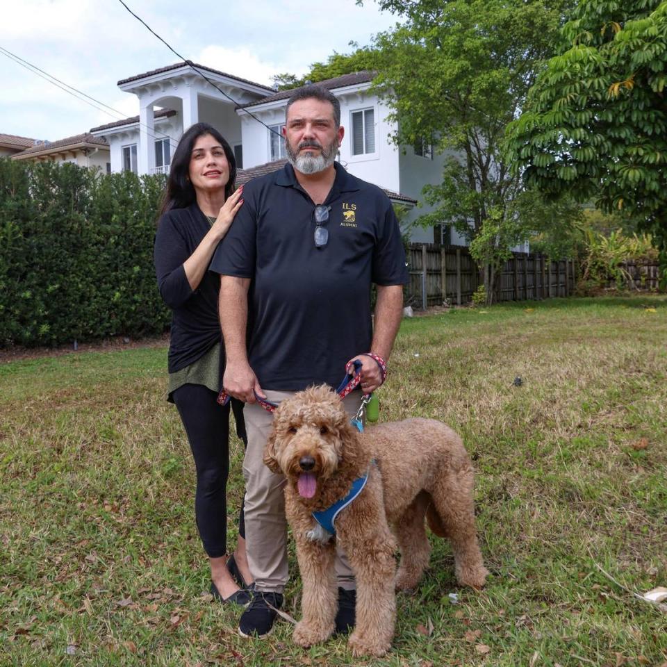 Bárbara Pazos y su esposo, José Pazos, propietarios de una vivienda en Schenley Park, frente al terreno baldío junto a su casa, visible detrás de ellos, donde un urbanizador ha solicitado permisos para construir dos dúplex en el barrio unifamiliar en virtud de una norma de Miami-Dade diseñada para ayudar a aliviar la escasez de viviendas en el condado.