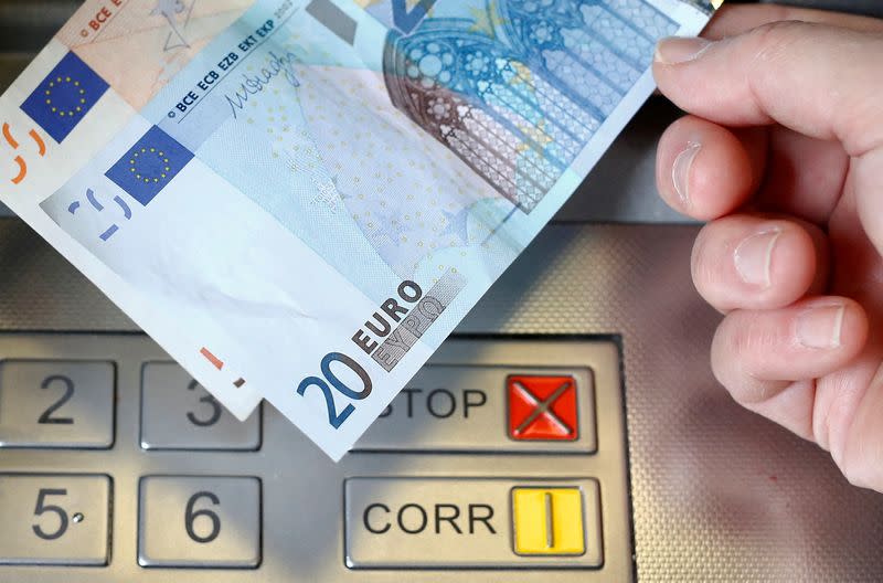 FILE PHOTO: A woman holds a 20 and 50 euro bank notes in front of an ATM in this illustration picture taken in Bern