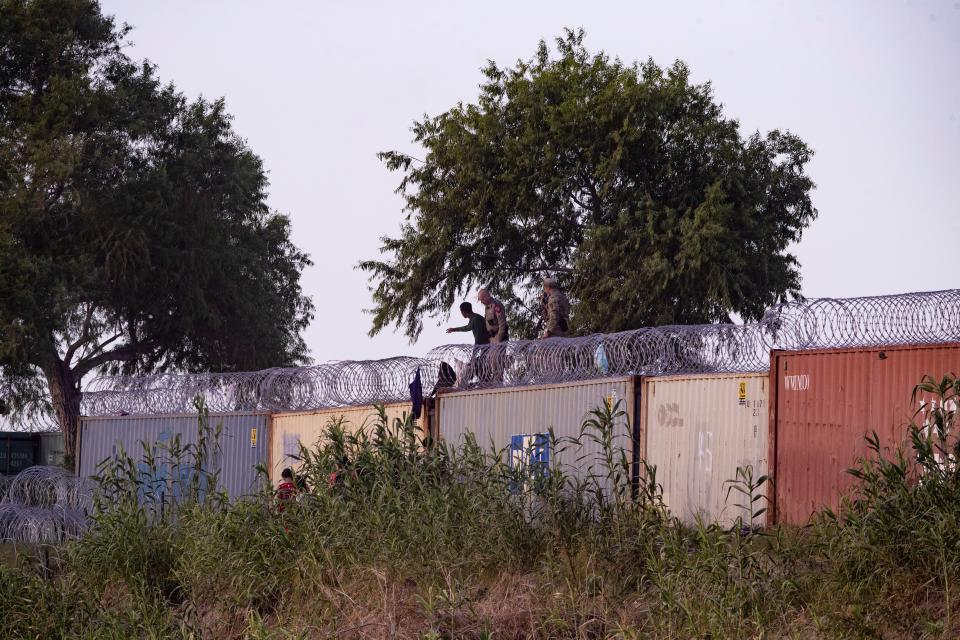 Migrants climb onto a shipping container set by state officials as an officer tells them to go back to the south side of the Rio Grande.