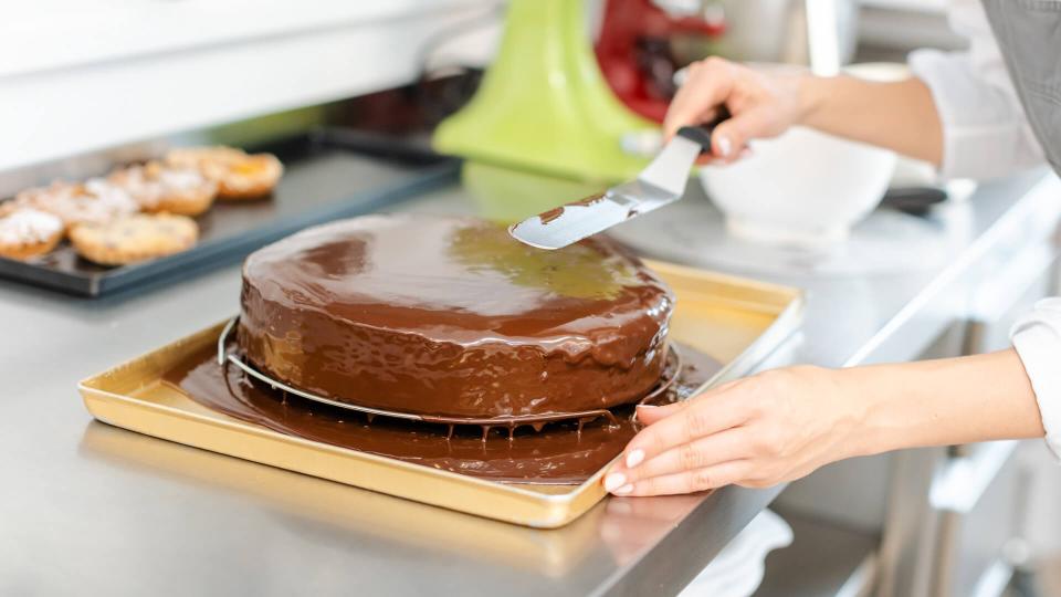 Patissier pouring liquid chocolate on a cake in her workshop.
