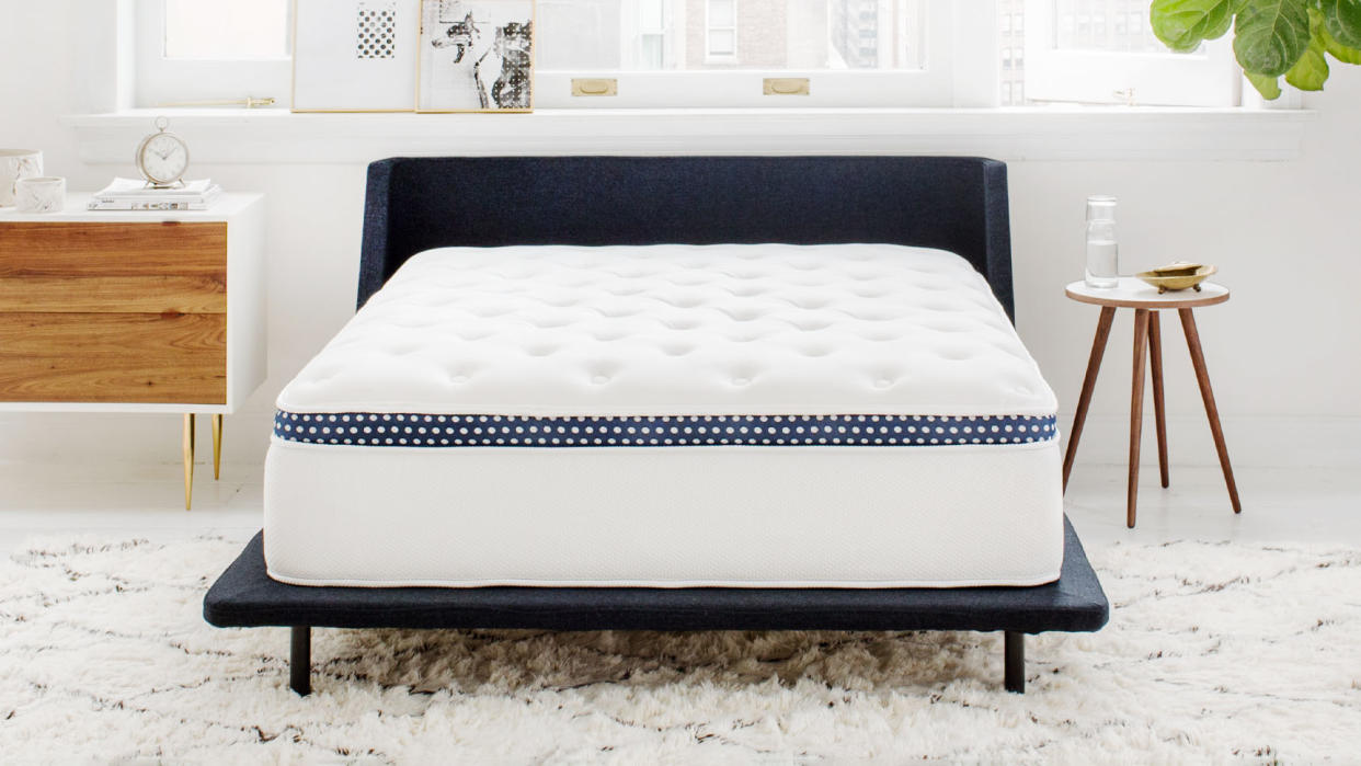  The WinkBed Mattress placed on a dark blue fabric bed frame and covered with a white comforter. 