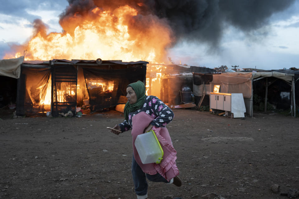 A woman runs past burning shacks during a fire before an eviction by police officers in Almeria, Spain, Monday, Jan. 30, 2023. A migrant camp in southern Spain's town of Nijar that was set to be demolished Monday has caught fire. Over 400 people live there, many working as temporary workers in farming estates. (AP Photo/Santi Donaire)