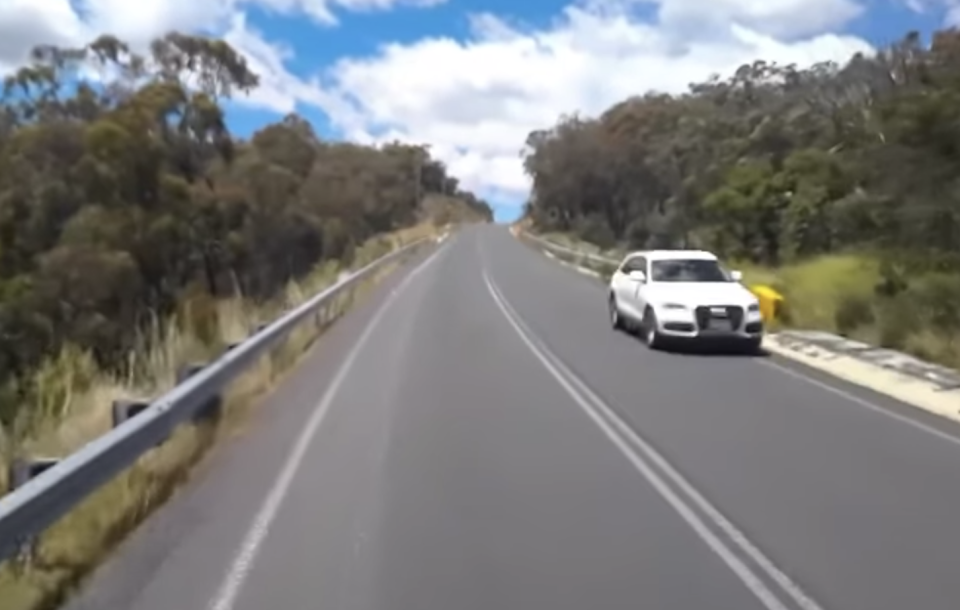 White car driving towards a truck, narrowly missing dangerous driver.