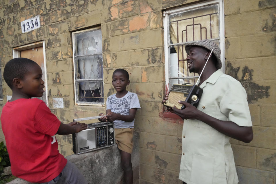 Ngwiza Khumbulani Moyo, a vintage collector, shows young boys some of his old radio sets outside his home in Bulawayo, Wednesday, Feb. 15, 2023. In many Western countries, conventional radio has been overtaken by streaming, podcasts and on-demand content accessed via smartphones and computers. But in Zimbabwe and much of Africa, traditional radio sets and broadcasts are widely used, highlighting the digital divide between rich countries and those where populations struggle to have reliable internet. (AP Photo/Tsvangirayi Mukwazhi)