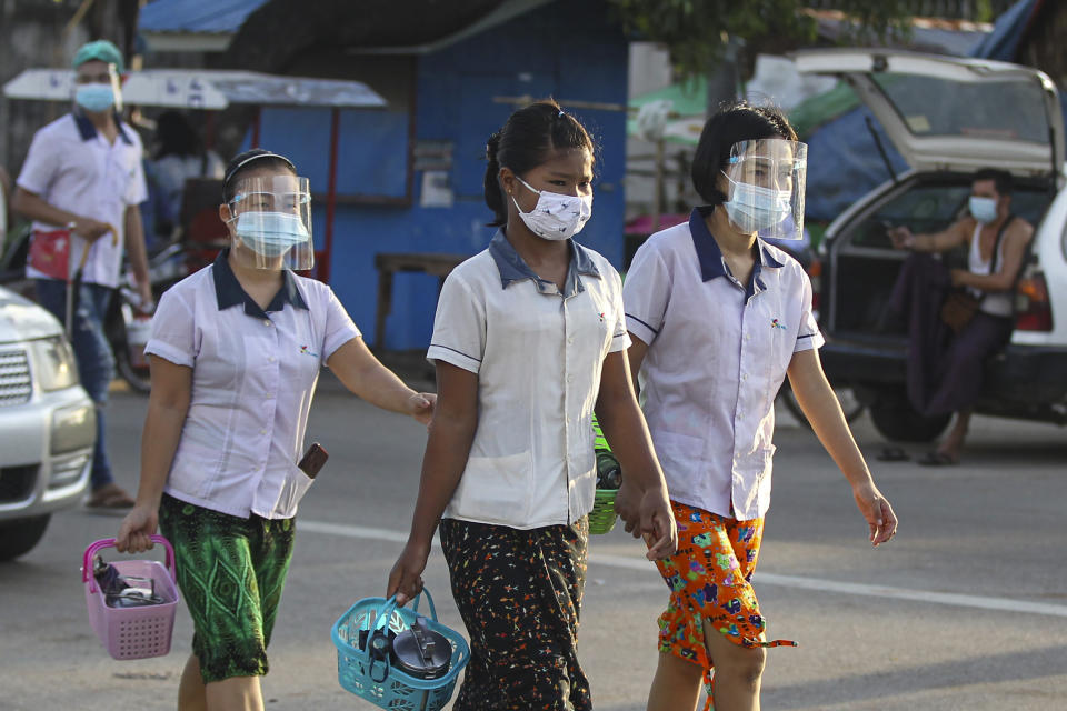 Factory workers wearing protective face masks and shields cross a road as they go to work in Hlaing Tharyar Industrial Zone Monday, Oct. 12, 2020, on the outskirts of Yangon, Myanmar. Myanmar government allowed Monday to resume Cut-Make-Pack (CMP) factories, workplaces and SMEs that meet "A-level" practices in COVID-19 containment measures by authorities even though higher numbers of positive cases found daily. Myanmar reached over 20,000 confirmed cases and more than 600 death with COVID-19. (AP Photo/Thein Zaw)