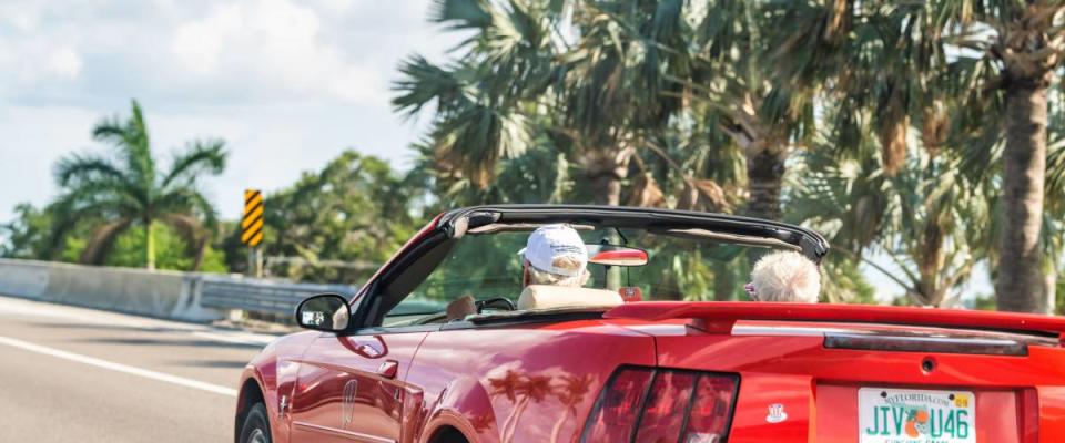 Ellenton, USA - April 27, 2018: Senior couple driving on sports car on road, highway with palm trees in Florida