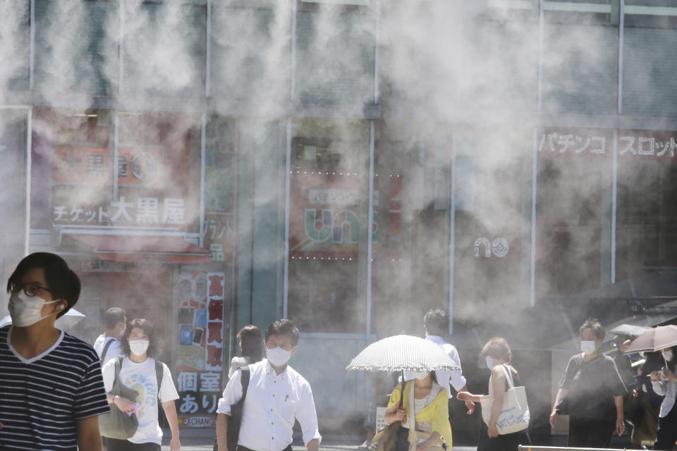 People wearing face masks to help protect against the spread of the coronavirus walk under a cooling water mist during the heat of the day in Tokyo Thursday, Aug. 5, 2021. (AP Photo/Koji Sasahara)