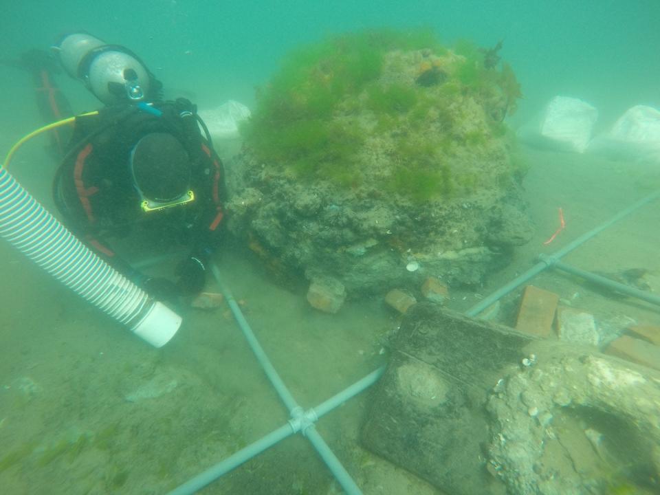 In deeper water near the wreck, next to the diver lies the heavily encrusted, upside-down remains of an iron cauldron, along with bricks from what might have been an oven used to heat blubber. Object to the right may have been a hawse pipe on the deck, where anchor chains passed through.