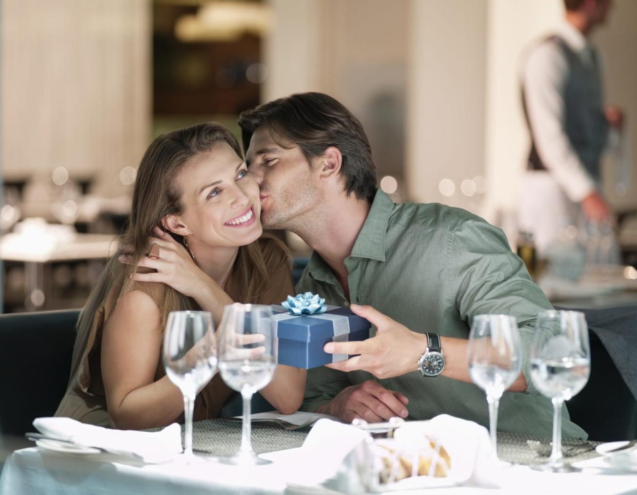 Man kissing and giving gift to woman in restaurant