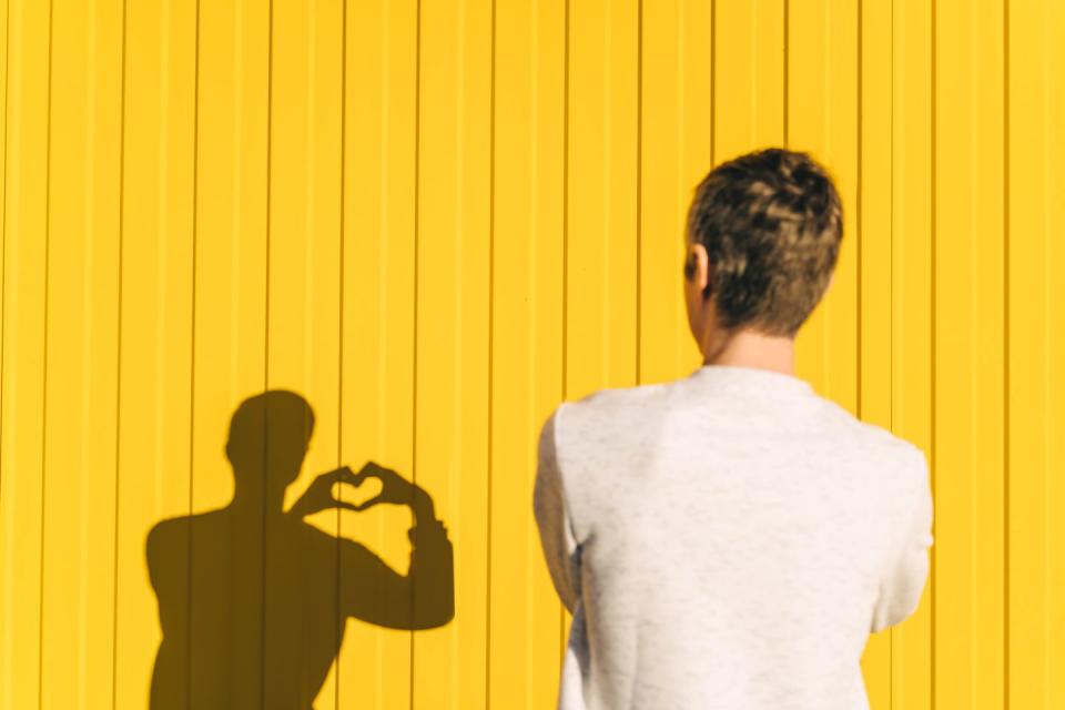 man makes heart shape with hand on yellow background, rear view
