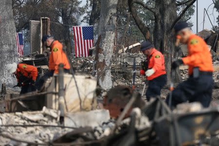 American flags hang behind search and rescue personnel in the aftermath of the Tubbs Fire in the Coffey Park neighborhood of Santa Rosa, California U.S., October 17, 2017. REUTERS/Loren Elliott