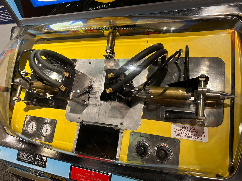 A closer look at the Mold-A-Rama mechanism and metal mold used to build the plastic space shuttle on Earth toy models.