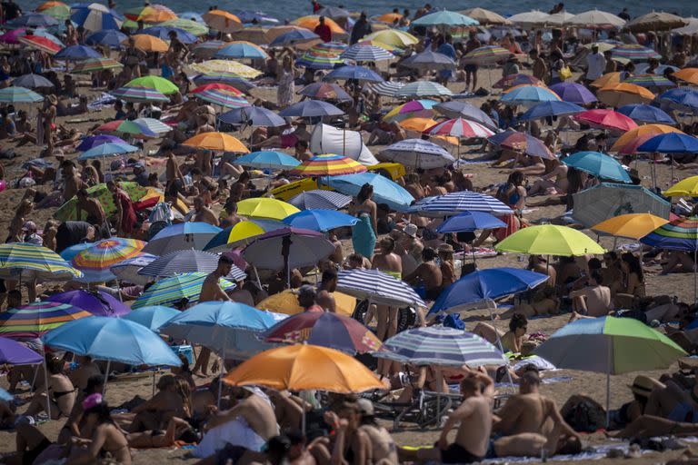 La gente usa sombrillas para protegerse del sol en la playa en un día caluroso y soleado en Barcelona, España, el viernes 15 de julio de 2022.