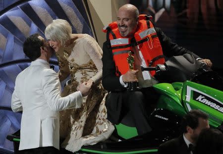 90th Academy Awards - Oscars Show - Hollywood, California, U.S., 04/03/2018 - Best Costume Design winner Mark Bridges rides a jet ski onto the stage as Oscars host Jimmy Kimmel gives actress Helen Mirren a kiss after Bridges won it for the shortest Oscar acceptance speech of 2018. REUTERS/Lucas Jackson