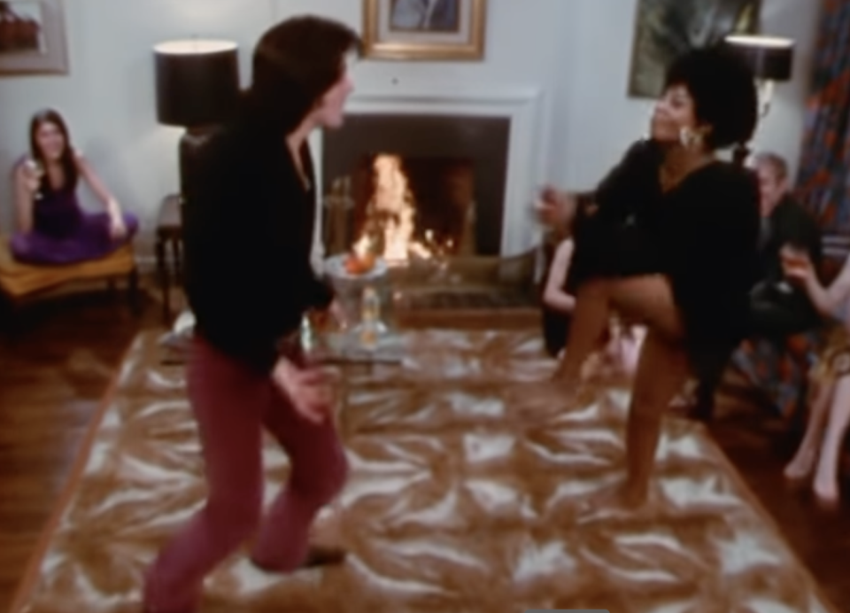 A screenshot of Sylvester Stallone dancing on a rug in a house that is the most 1970s setting you've ever seen