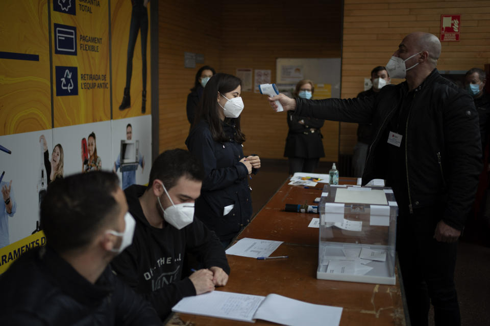 A woman working at a polling station set up in a market, is taken the temperature during the regional Catalan election in Barcelona, Spain, Sunday, Feb. 14, 2021. Over five million voters are called to the polls on Sunday in Spain's northeast Catalonia for an election that will measure the impact of the coronavirus pandemic on the restive region's secessionist movement. (AP Photo/Emilio Morenatti)