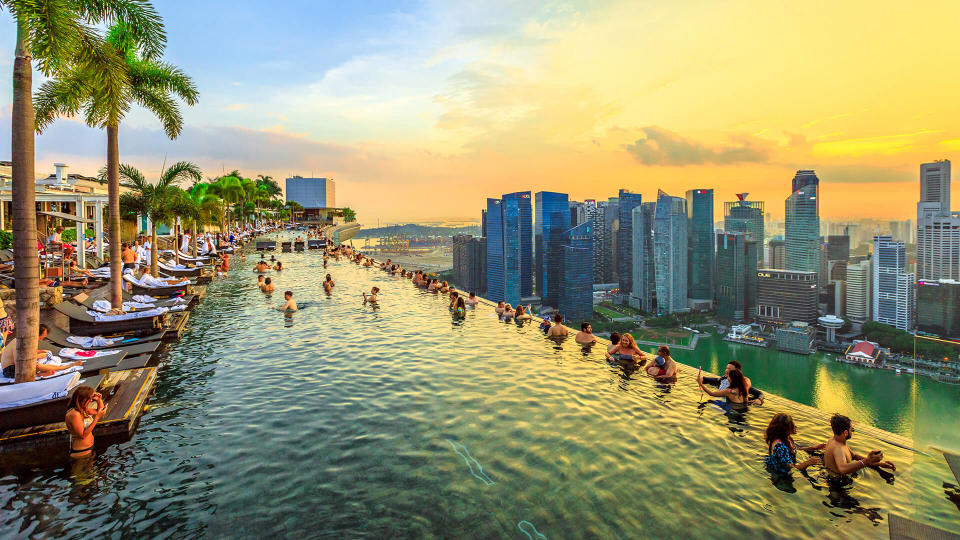 Infinity Pool at sunset of Skypark that tops the Marina Bay Sands Hotel and Casino from rooftop of La Vie Club Lounge on 57th floor. Financial district skyline on background