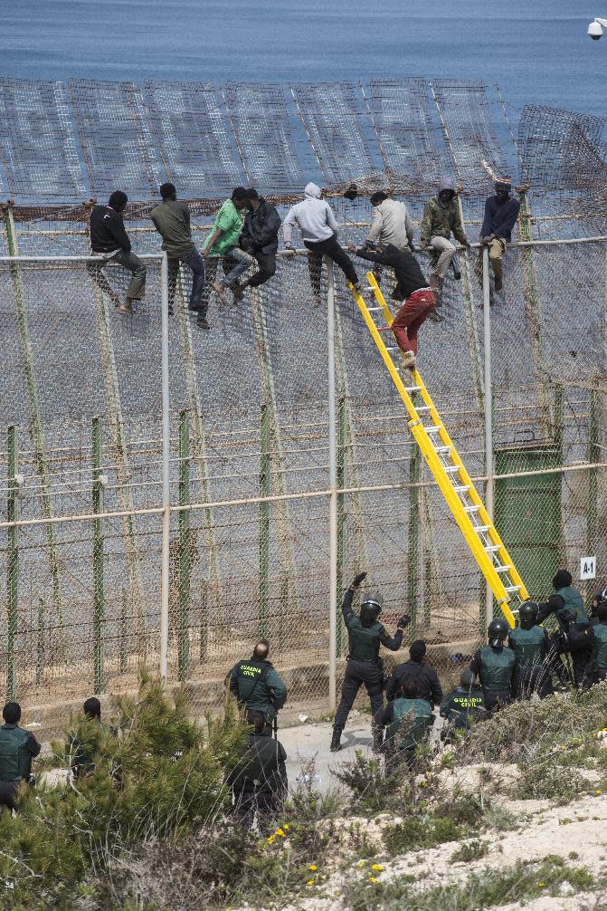 A sub-Saharan migrant climbs down a ladder held by Spanish Guardia Civil officers as other sit on top of a metallic fence that divides Morocco and the Spanish enclave of Melilla, Thursday, April 3, 2014. Spanish and Moroccan police have thwarted a fresh attempt by dozens of African migrants to try to scale border fences to enter the Spanish enclave of Melilla. Thousands of sub-Saharan migrants seeking a better life in Europe are living illegally in Morocco and regularly try to enter Melilla in the hope of later making it to mainland Spain. (AP Photo/Santi Palacios)