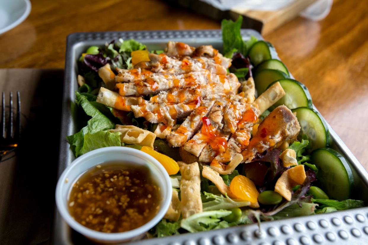 Sliced grilled chicken breast drizzled with dressing, fried noodles and tangerines on a healthy salad