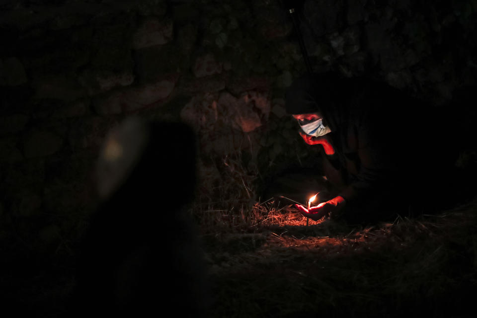 An orthodox worshiper, wearing a mask for protection against the COVID-19 virus, holds a candle while sitting in an open archaeological site outside the Cathedral of Saints Peter and Paul, which includes ruins dating as far back as the Roman Empire, during a religious service in the Black Sea port of Constanta, Romania, Wednesday, May 27, 2020. Romanian Orthodox Archbishop Teodosie rescheduled the Orthodox Easter service, which was to be held in mid-April, to offer worshippers an opportunity to celebrate Easter properly after the cancelling of the original April 19 service due to the national lockdown imposed because of the coronavirus epidemic. (AP Photo/Vadim Ghirda)