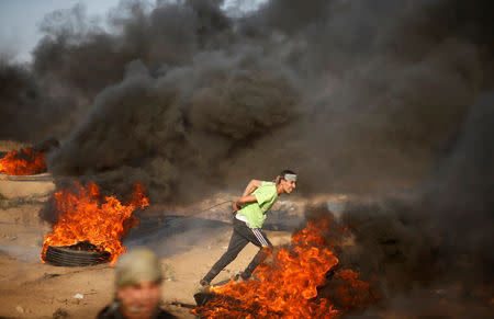 A Palestinian demonstrator pulls a burning tyre during a protest calling for lifting the Israeli blockade on Gaza and demanding the right to return to their homeland, at the Israel-Gaza border fence east of Gaza City September 28, 2018. REUTERS/Mohammed Salem