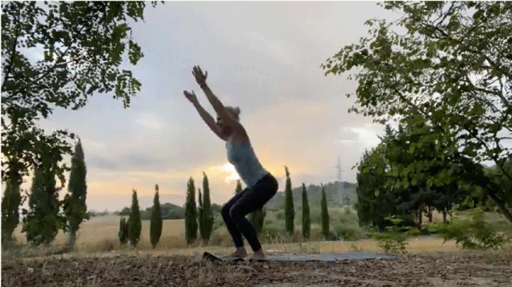Woman practicing yoga outside at sunrise with her knees bent and her arms alongside her ears