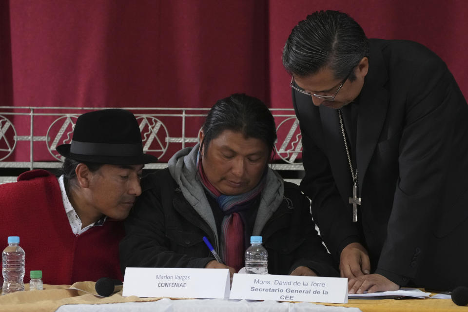 Indigenous leaders, Leonidas Iza, left, and Marlon Vargas, center, revise an agreement document with Monsignor David de la Torre during a dialogue session with the government, with Catholic Church representatives as mediador, at the Episcopal Conference headquarters in Quito, Ecuador, Thursday, June 30, 2022. The two groups are discussing solutions that could lead to the end of a strike over gas prices that has paralyzed parts of the country for two weeks. (AP Photo/Dolores Ochoa)