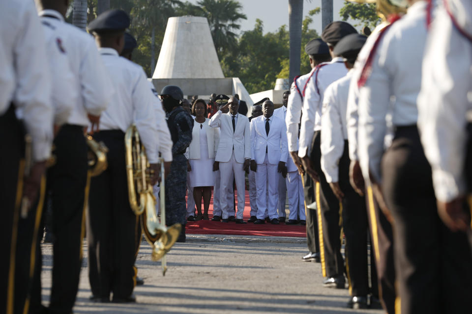 Accompanied by First Lady Martine Moise, center left, President Jovenel Moise salutes a police marching band before laying flowers to mark the anniversary of the death of Haitian revolution leader Jean Jacques Dessalines, at Champ de Mars, adjacent to the National Palace, in Port-au-Prince, Haiti, Thursday Oct. 17, 2019. President Moise has been facing ever more violent protests demanding his resignation fueled by anger over corruption, inflation and dwindling of basic supplies, including gasoline. (AP Photo/Rebecca Blackwell)