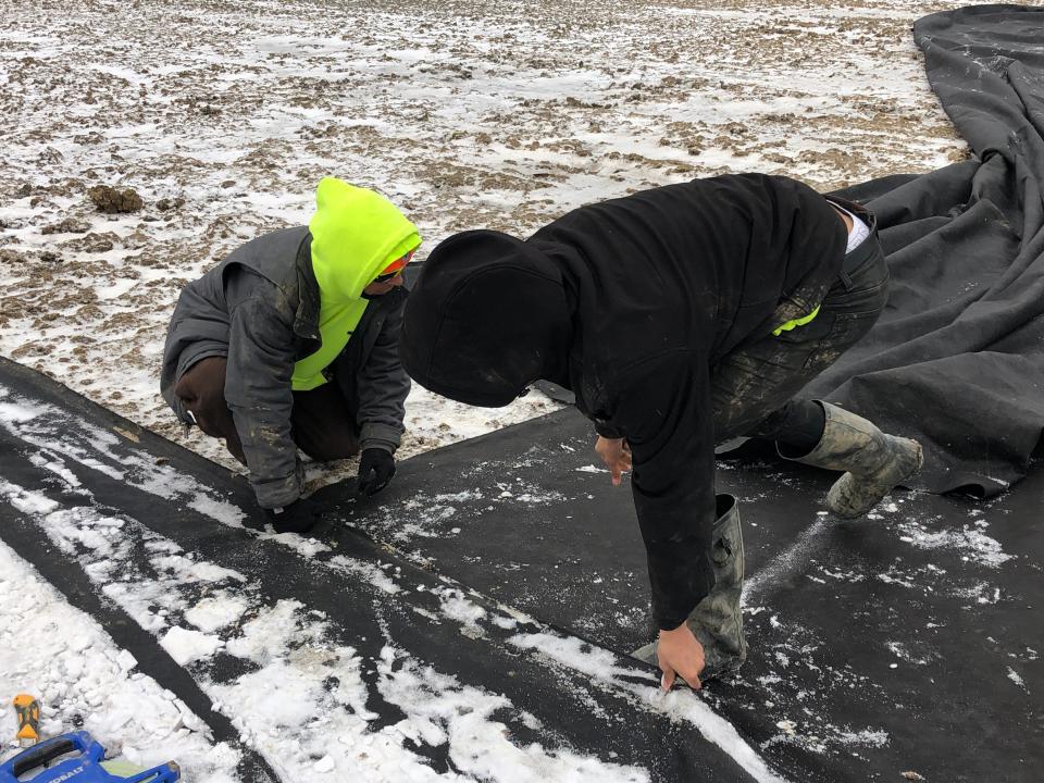 SCG Fields employee William Howell teaches Alliance High senior Tyion Miles how to properly install cloth on a dirt surface before putting gravel on it at the school's baseball field.