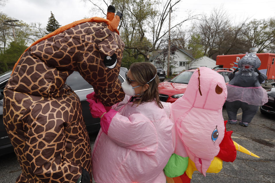 In this Monday, May 11, 2020 photo, Sarah Ignash helps a member of the T-Rex Walking Club with a giraffe costume in Ferndale, Mich. The group takes its unannounced strolls through neighborhoods on a quest to bring smiles to the faces of kids, and a few adults, while under Michigan's stay-at-home order because of the COVID-19 pandemic. (AP Photo/Carlos Osorio)