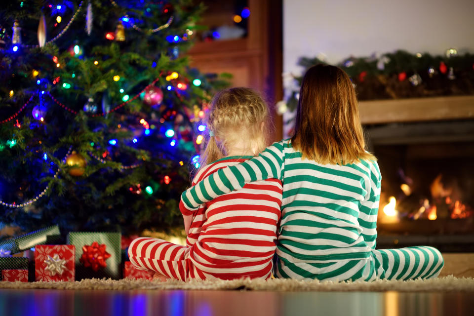 Happy little sisters wearing Christmas pajamas opening gift boxes by a fireplace in a cozy dark living room on Christmas eve. Celebrating Xmas at home.