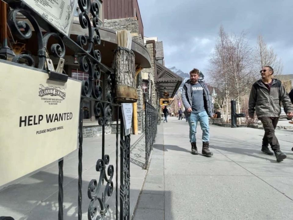 A help wanted sign is pictured Banff, Alta. as pedestrians look on. Amid a persistently tight labour market, some businesses are having to work harder to convince job seekers to apply. (Bryan Labby/CBC - image credit)