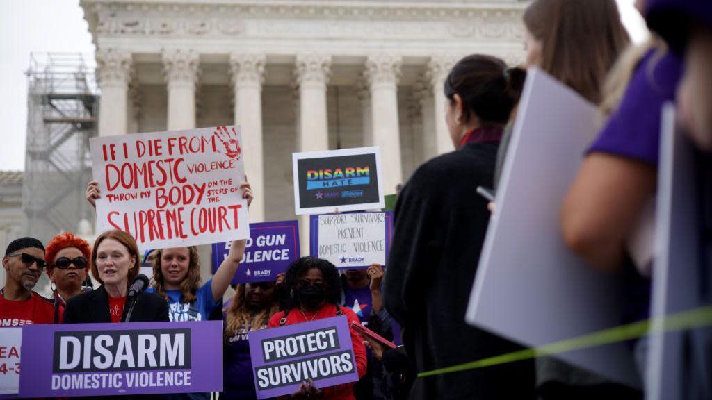 Crowd holding signs against domestic violence, Julianne Moore at podium with microphone