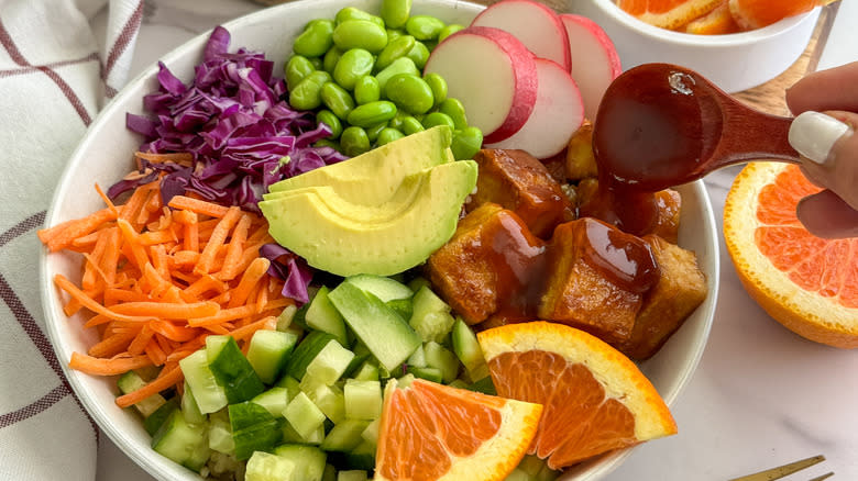 hand adding sauce to tofu and vegetable bowl