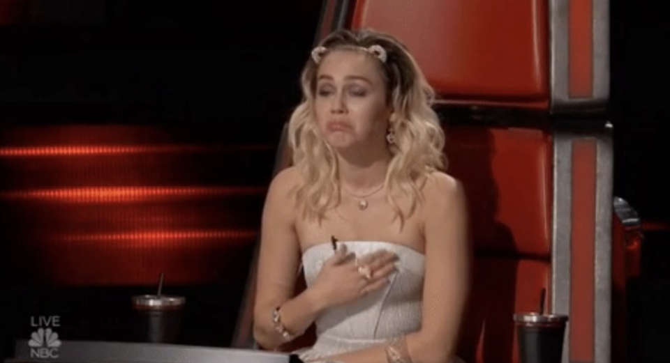 Miley Cyrus making an "aww" face and putting her hand on her heart