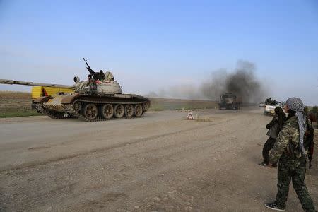 A military tank is driven past Kurdish People's Protection Units (YPG) and Kurdistan Workers Party (PKK) fighters manning a checkpoint on a highway connecting the Iraqi-Syrian border town of Rabia and the town of Snuny, north of Mount Sinjar December 20, 2014. REUTERS/Massoud Mohammed